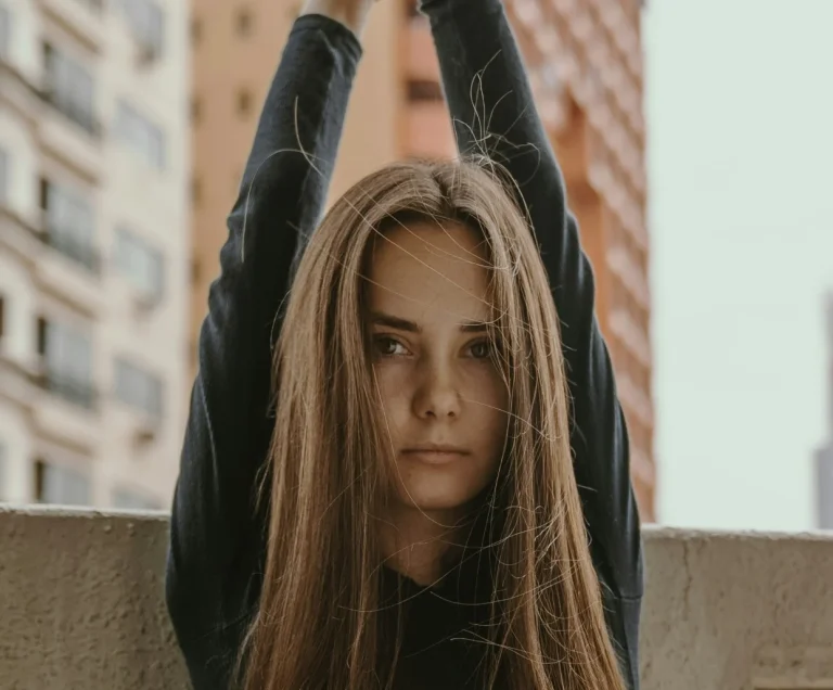 A young woman sits in a chair and raises her hands above her head.