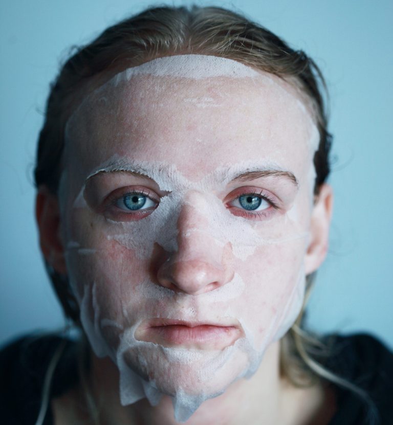 A young woman looks into the camera with a skincare mask on