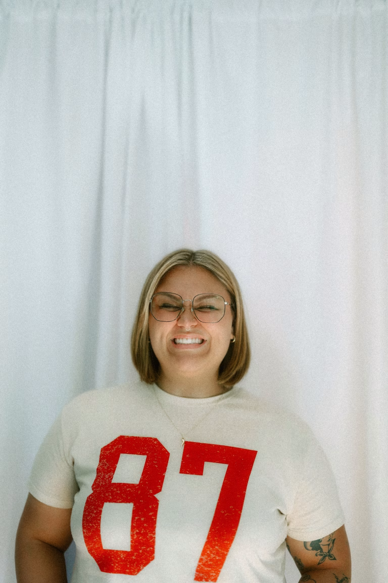 Woman smiles at the camera, wearing glasses and football shirt