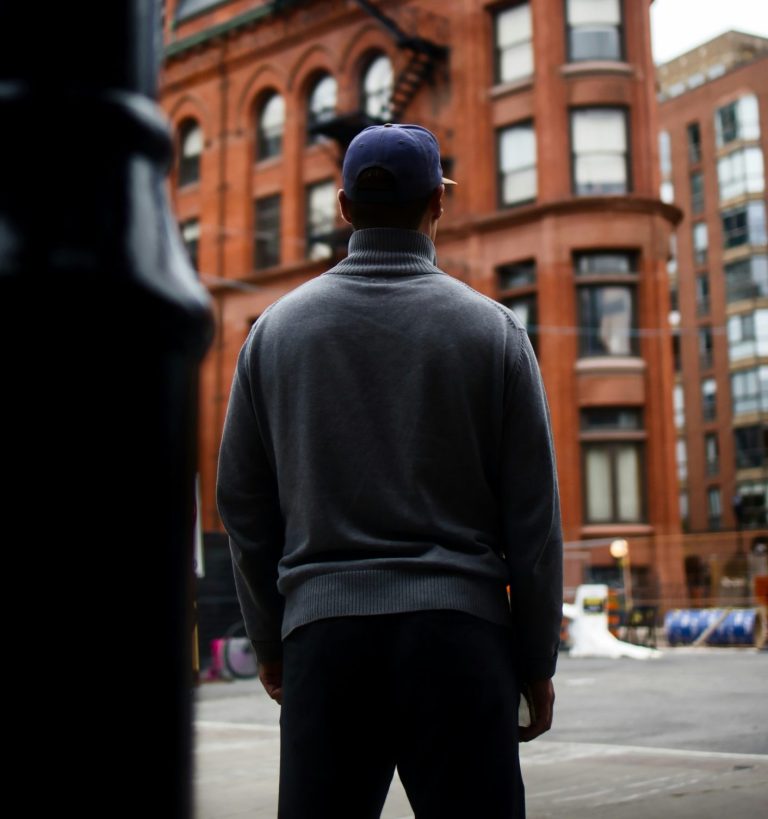 A man in a hat stands on the street and admires an old building.