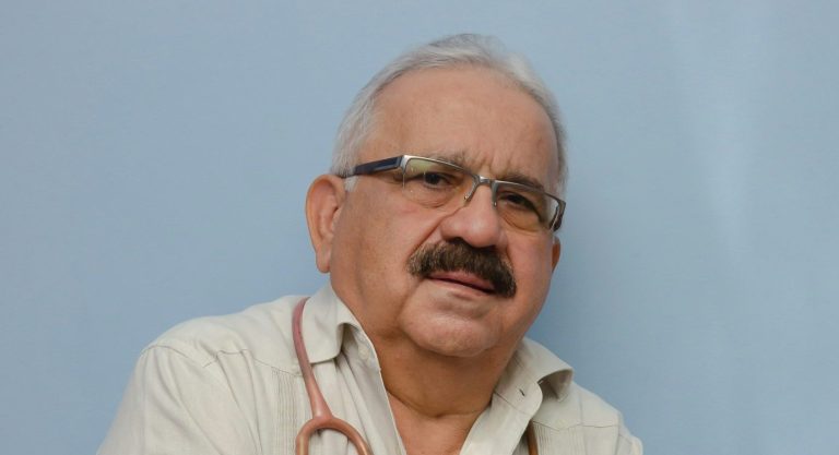 An older Mexican doctor crosses his arms and smiles.