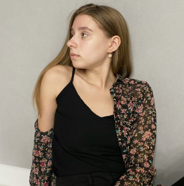 A young woman in a black tank top looks to the side.