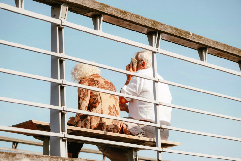 Elderly couple on cruise ship sitting next to each other on a bench.