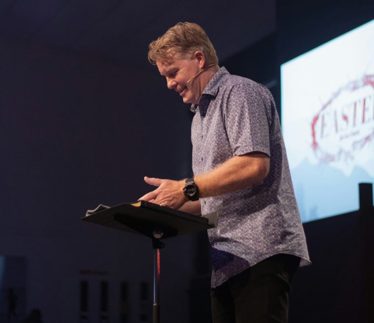 A pastor in a collared shirt gives a sermon on stage